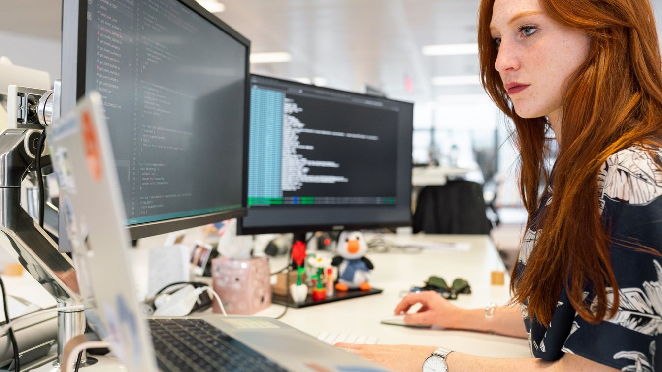 A developer working across dual monitors and a laptop in a modern office
