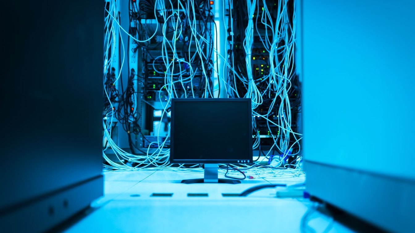A tangle of network cables behind server racks in a data center, lit in blue