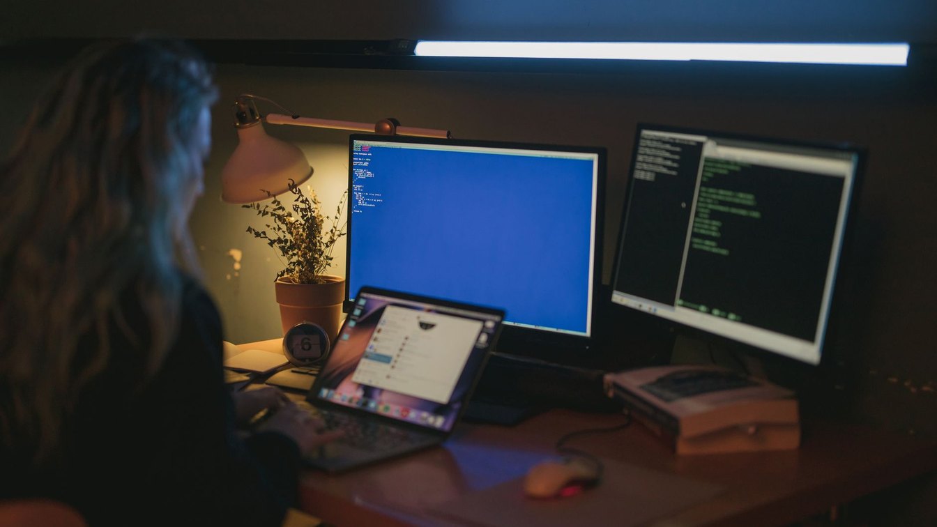 An engineer working across multiple monitors with code and dashboards at night