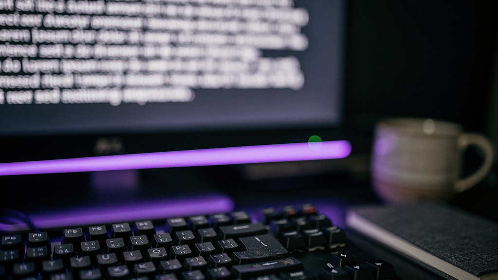 A developer's desk at night, monitor thrown into soft bokeh showing only the implied shape of a dense prose paragraph, lit by a single violet LED